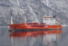 A large gas carrier ship, the Coral Electra, sails on calm blue waters under a clear sky.