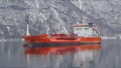 A large gas carrier ship, the Coral Electra, sails on calm blue waters under a clear sky.