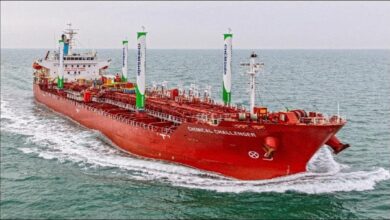 A chemical tanker with a tall white wing sail sails on calm waters.
