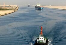 A large container ship laden with colorful containers sails on calm open water.