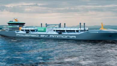 A large cargo ship receives bio-methanol fuel from a bunkering vessel near an industrial port.