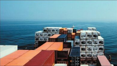 A large containership with stacked containers sails on the open sea under a cloudy sky.