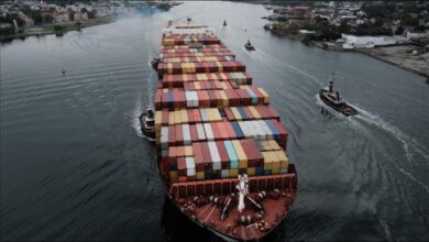 A large container ship fully loaded with cargo containers sails on the ocean.
