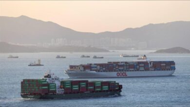 A massive container ship filled with cargo containers sails across the water.
