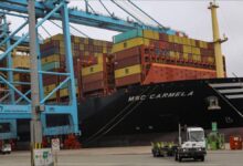 A container ship is loaded by large cranes at a busy port terminal.