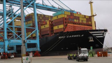 A container ship is loaded by large cranes at a busy port terminal.