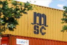 A large MSC container ship sails through calm blue waters.