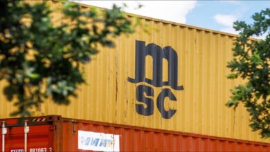 A large MSC container ship sails through calm blue waters.