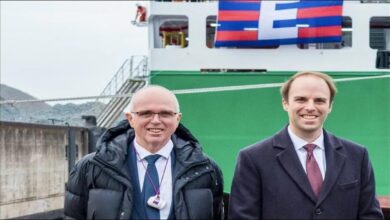 A large container ship, stacked with colorful containers, sails on the water.
