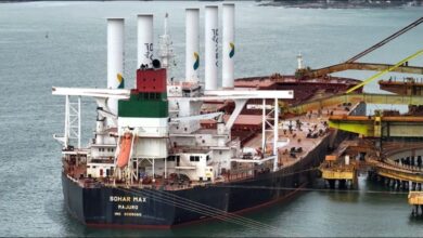 Large cargo ship at sea with multiple cylindrical rotor sails for wind-assisted propulsion.
