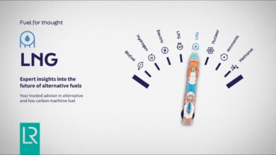 A large LNG-powered cargo ship sails past a port, accompanied by two smaller boats.