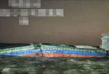 A large cargo ship emits heavy smoke from its midsection, with a rescue vessel positioned nearby.