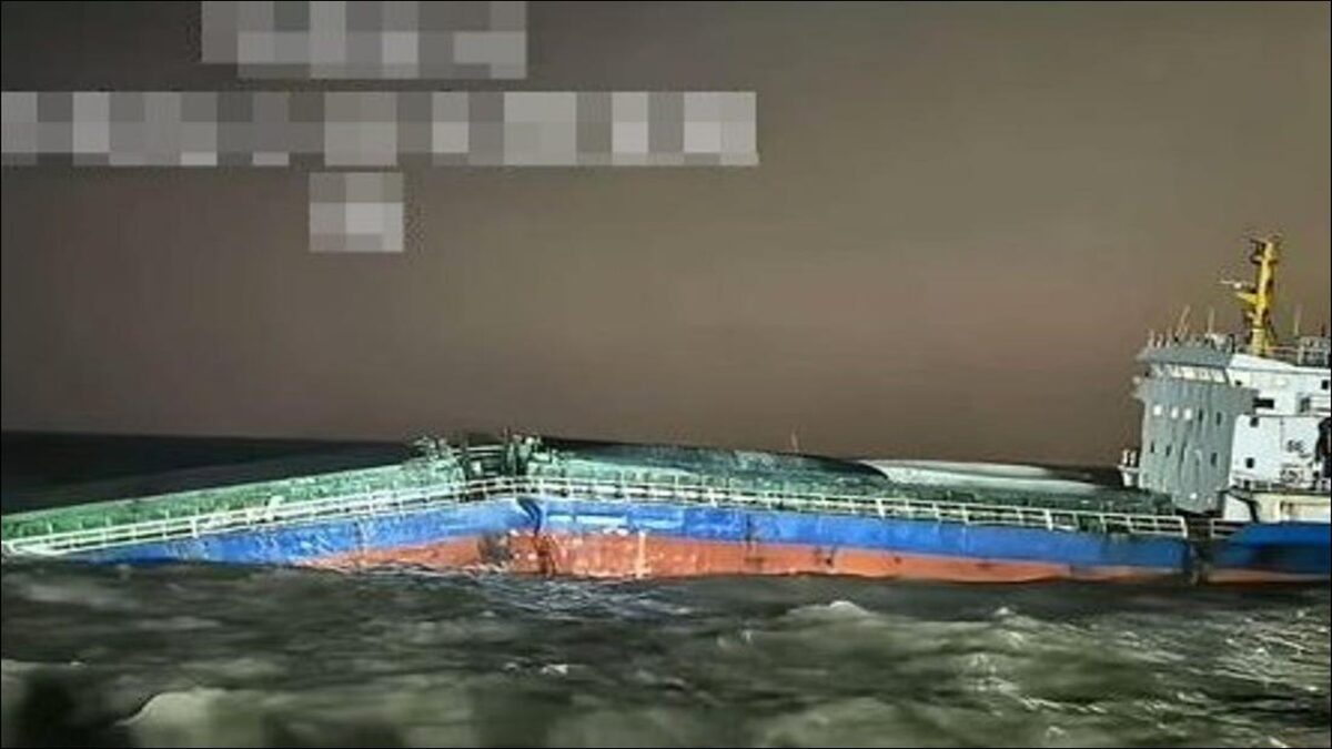 A large cargo ship emits heavy smoke from its midsection, with a rescue vessel positioned nearby.