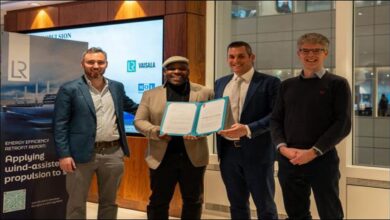 A large cargo ship at sea with multiple modern wind propulsion sails deployed on deck.
