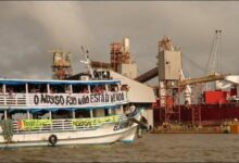Indigenous activists unfurl protest banners on a grain barge at a river terminal.