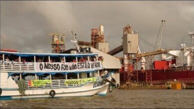 Indigenous activists unfurl protest banners on a grain barge at a river terminal.