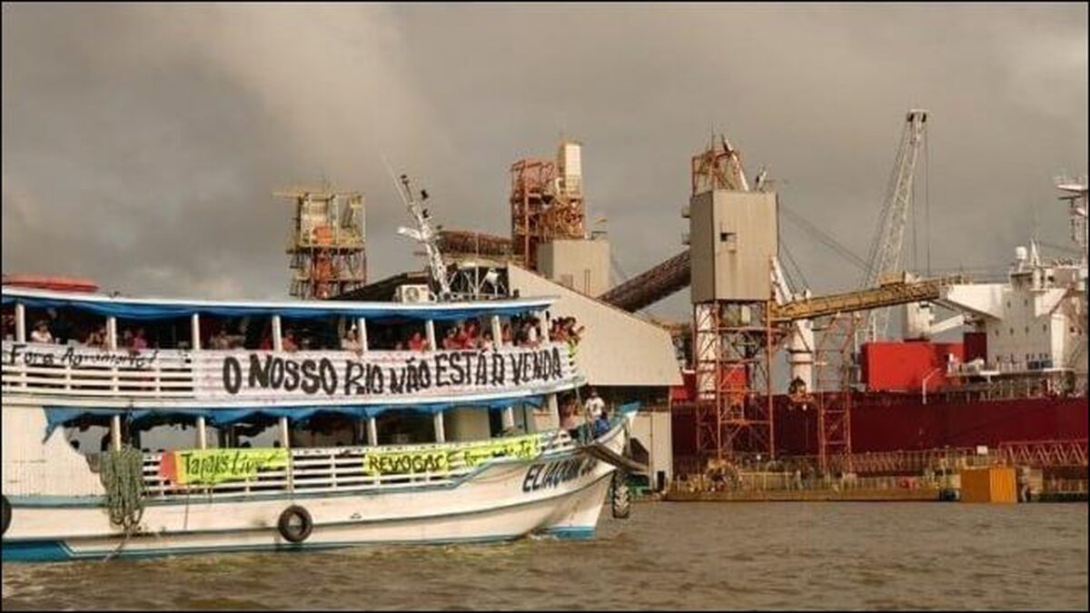 Indigenous activists unfurl protest banners on a grain barge at a river terminal.