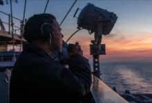 A commercial container ship on the sea with a warship, reflecting maritime security concerns.
