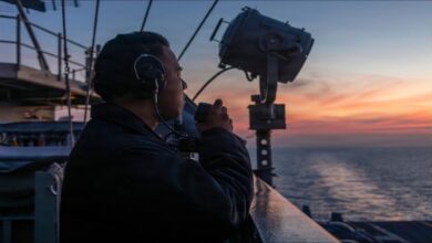 A commercial container ship on the sea with a warship, reflecting maritime security concerns.