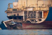 Workers dismantle a large vessel on a shipbreaking beach.