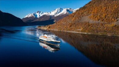 Havila Kystruten ship navigating a scenic Norwegian fjord.