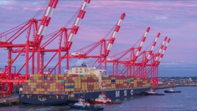 A massive container ship, an ocean carrier, sails through a busy port during daytime.