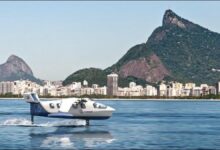 A white Regent electric Seaglider flies over blue water near a tropical coast.
