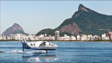 A white Regent electric Seaglider flies over blue water near a tropical coast.