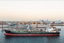 A large tanker ship receives marine fuel from a bunkering vessel at a port.