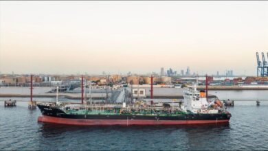 A large tanker ship receives marine fuel from a bunkering vessel at a port.