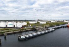 An industrial port terminal with numerous large storage tanks and docked ships in Rotterdam.