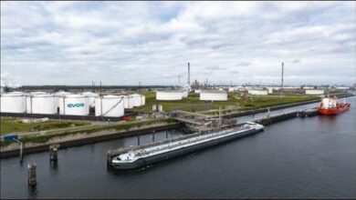 An industrial port terminal with numerous large storage tanks and docked ships in Rotterdam.