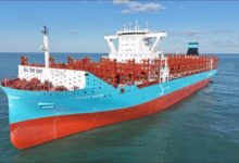 A large blue Maersk container ship docked at a busy port for global shipping.