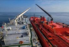 A bunkering vessel fuels a large cargo ship in a busy port at sea.