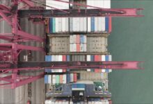 A large container ship loaded with colorful containers sails on the ocean.