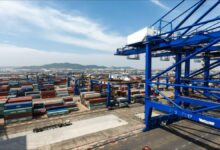 A large container ship is moored at a modern port terminal with cranes.