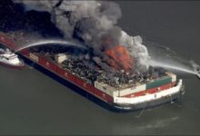 Large scrap fire on a barge in the Delaware River emitting thick black smoke.