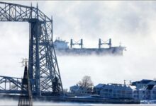 A large freighter pushes through thick ice on Lake Superior, delaying maritime shipping.