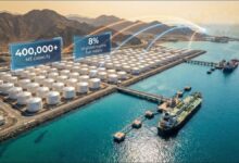 A large vessel docked at an industrial port with fuel storage tanks.