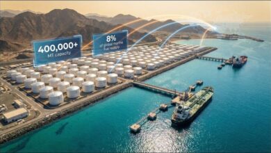 A large vessel docked at an industrial port with fuel storage tanks.