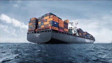 A large Hapag-Lloyd container ship carries cargo through a port.