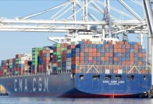 A large CMA CGM container ship sails across blue water, loaded with cargo containers.