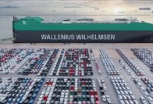 A large Wallenius Wilhelmsen car carrier ship sails on open water under a clear sky.