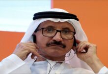 A large container ship docked at a busy port terminal with cranes and stacked containers.