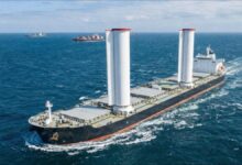 A cargo ship with three white Flettner rotor sails cruises on the open sea.