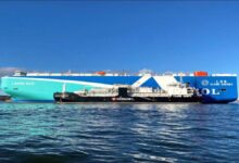 A large cargo ship receives LNG bunkering fuel from a tanker vessel in a port.