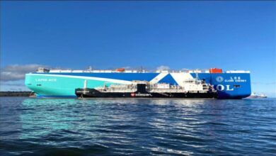 A large cargo ship receives LNG bunkering fuel from a tanker vessel in a port.