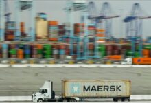 Maersk shipping containers are stacked near a large Maersk cargo ship at a port.