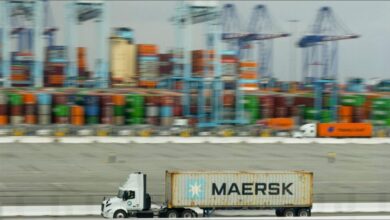 Maersk shipping containers are stacked near a large Maersk cargo ship at a port.