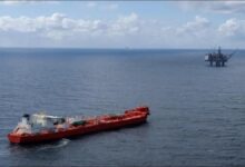 An offshore gas drilling rig stands in calm seas with a support vessel nearby.